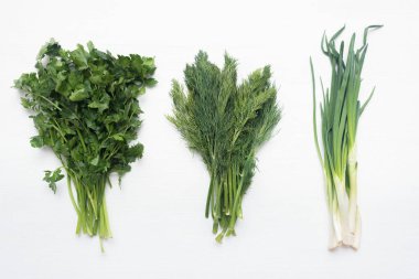Beyaz arka planda dereotlu soğan ve maydanoz gibi yeşillik yığınları.