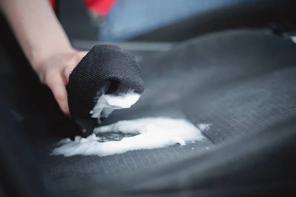 Cleaner is cleaning a car seats with foam cleaner close up.