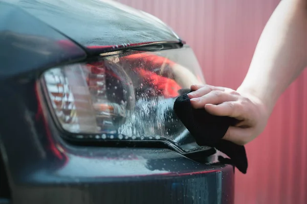 Cleaner is cleaning a car headlights with a rag close up.