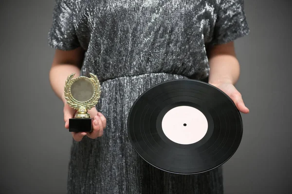 Music award ceremony concept. A singer with golden award trophy and vinyl record in hands on gray background.