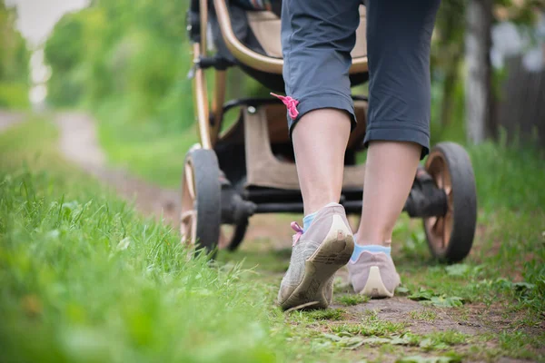 若い女性は公園で赤ちゃんの馬車と歩いています — ストック写真