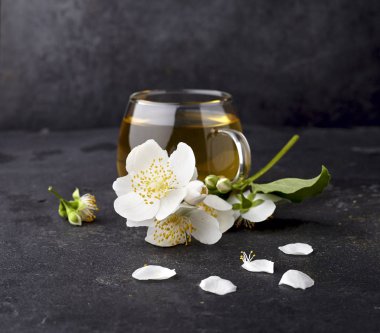 Bir fincan yeşil çay ve siyah arka planda yasemin çiçekleri. Bitki