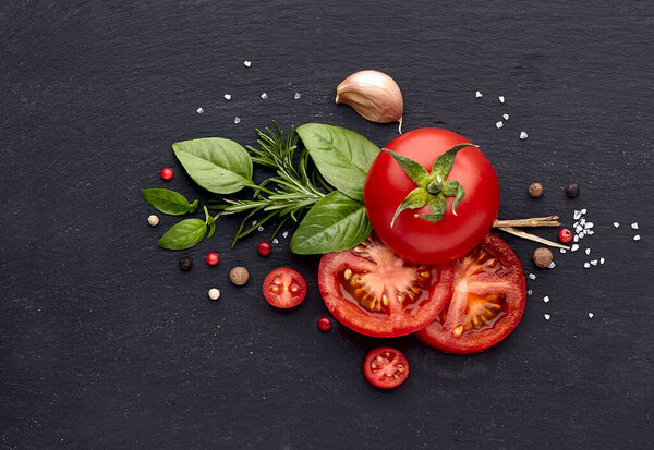 Fresh basil leaves with tomatoes, pepper, rosemary and garlic on black stone background. Top view.