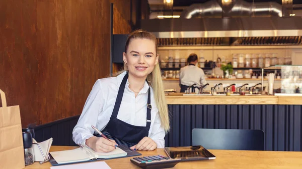 Gülümseyen güzel bir kadın, küçük bir aile restoranında oturmuş, çalışmalarının finans faturalarını hesaplarken iş kadını dijital tablet ve hesap makinesi kullanıyor..