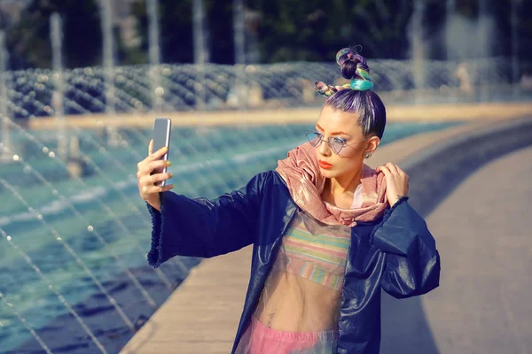 Çılgın saçlı ve yenilikçi stili olan havalı hippi genç moda etkileyicisi kız sokakta selfie çekiyor - kadın yayın platformu ve sosyal medya platformunda moda içeriğini paylaşıyor