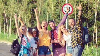 Group of best friends having fun taking selfie with raised arms during travel adventure in countryside
