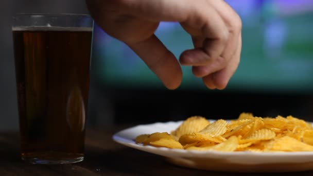 Una mano de hombre toma papas fritas y cerveza de la mesa, en la televisión va el fútbol — Vídeos de Stock
