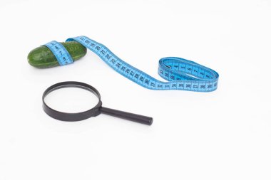 Cucumber with a measuring tape and a magnifying glass on a white background. Genital size concept in a man, penis enlargement
