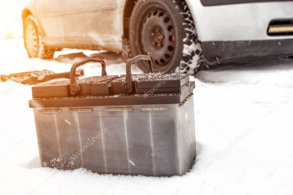 Car battery against the background of a car in winter. Winter battery discharge concept, copy space