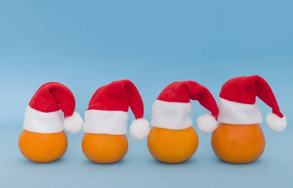 Плоды мандаринов в маленьких рождественских шапочках Санта Клауса на синем фоне. Новогодние и рождественские праздники. Место для текста, место для копирования — стоковое фото