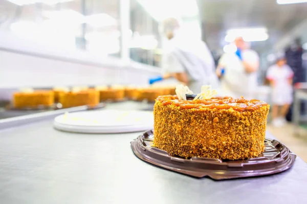 Οι εργάτες ζαχαροπλαστικής φτιάχνουν κέικ μπισκότων με φφολιάτες με συμπυκνωμένο γάλα και δαμάσκηνα. Παραγωγή γλυκών και επιδόρπια. Βιομηχανία τροφίμων, αντιγραφή χώρου — Φωτογραφία Αρχείου