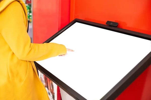Дівчина в жовтому пальто натискає пальцем на електронний дотик онлайн табло. Концепція довідкової інформації та електронної черги в банках та клініках, станції, копіювання простору — стокове фото