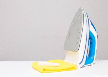 Sarı bir bez ve temiz bir kalemle bir ütü beyaz bir arkaplanda bir masanın üzerinde duruyor. Demir taban temizleme konsepti, kopyalama alanı, ev ödevi