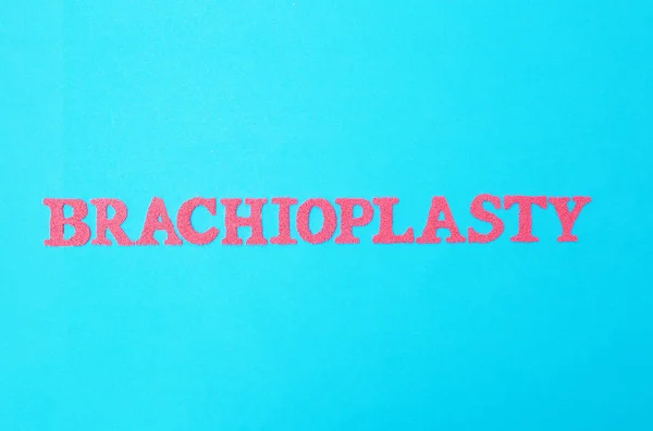 The word brachioplasty in red letters on a blue background. The concept of the modern procedure in plastic surgery for lifting the skin on the hands of a person, medical — Stock Photo, Image
