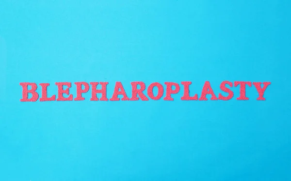 Blefaroplastia de palabras en letras rojas sobre fondo azul. El concepto de cirugía plástica involucrado en el levantamiento de la piel de los párpados inferior y superior, la eliminación de la inflamación y las arrugas alrededor de los ojos —  Fotos de Stock