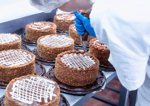 Ο ζαχαροπλάστης διακοσμεί την τούρτα με τη βοήθεια κρέμας. Κέικ στην παραγωγή, βιομηχανία τροφίμων, torte — Φωτογραφία Αρχείου