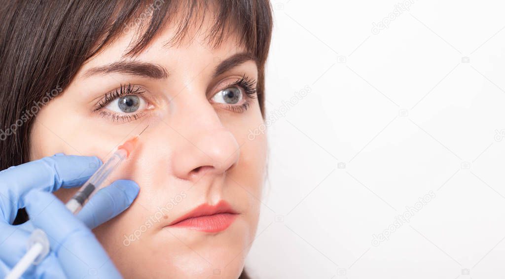 A cosmetologist doctor gives the girl an injection of rejuvenation under the eyes. The concept of rejuvenation and elimination of bags and bruises under the eyes, copy space