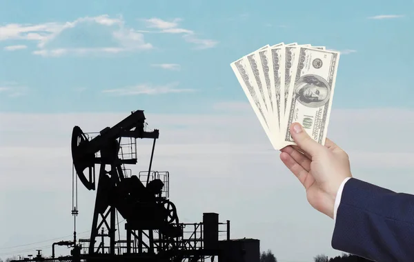 Muž drží v ruce peníze na pozadí studny, která produkuje ropu a plyn. Koncept ropného hospodářství a růst cen ropy a zemního plynu, průmyslu — Stock fotografie