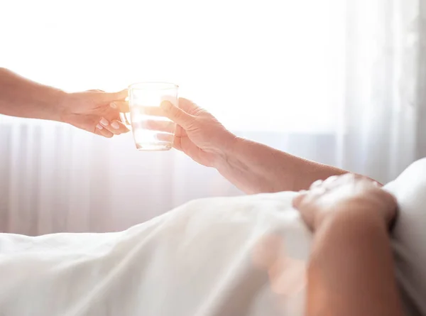 Le travailleur social donne à une femme âgée handicapée une tasse d'eau sur le fond d'une fenêtre avec le soleil. Le concept de prise en charge des personnes âgées et handicapées, service, espace de copie — Photo