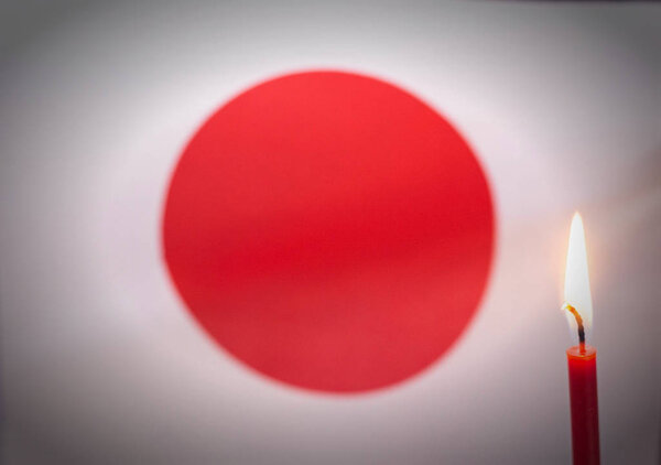 Burning candle on the background of the flag of Japan. The concept of mourning and sorrow in the country, terrorism