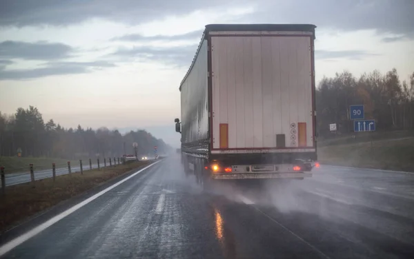 A truck with a trailer is being rebuilt on a motorway in a different row on slippery wet roads. The concept of security and attention to roads in bad weather, rain — Stock Photo, Image