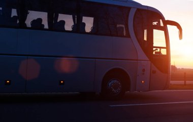 Modern comfortable passenger bus against the background of the orange sky with sunset rides on the highway. The concept of travel in Europe and passenger transportation in travel companies, discount