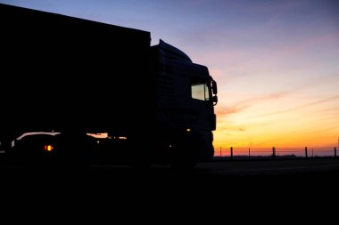 Karavanı olan bir kamyon gece otoyolda turuncu güneşli bir günbatımının arka planına doğru gidiyor. İş rejimi kavramı ve diğer kamyoncular, kopyalama alanı, tachograph
