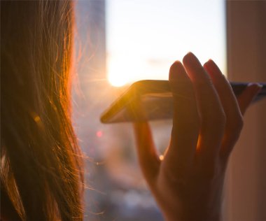 Girl holds a smartphone in her hand on a background of sunny sunset. Concept phone application for people with disabilities, disabled, blind clipart