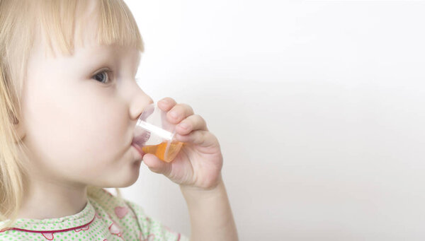 Маленькая девочка пьет сироп от кашля в мерной чашке для детей. Концепция лечения бронхита и пневмонии лекарственным сиропом у детей, копировальное пространство
