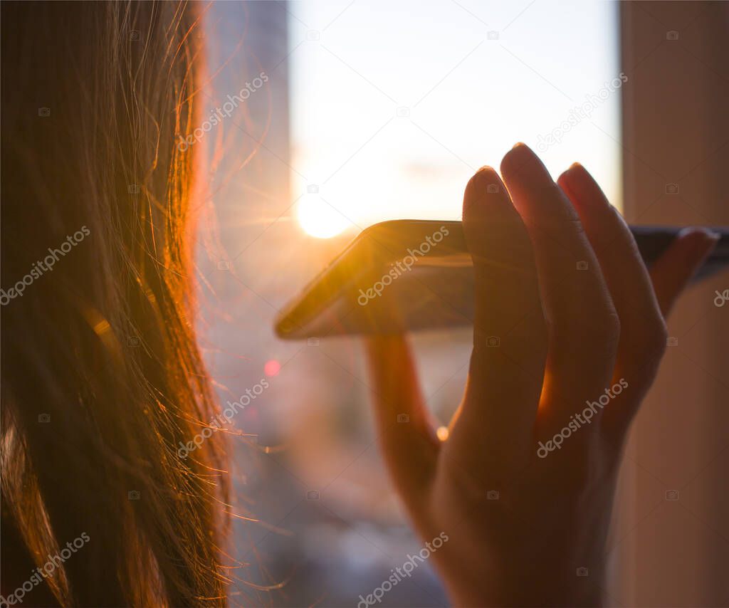 Girl holds a smartphone in her hand on a background of sunny sunset. Concept phone application for people with disabilities, disabled, blind