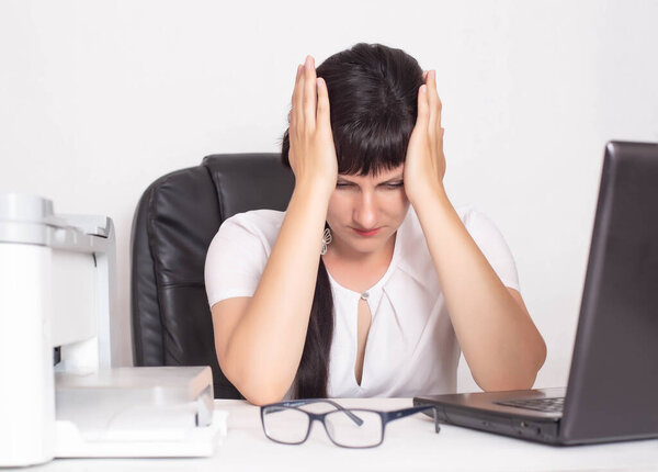 A girl sits in a business office and holds on to her head. The concept of crisis and decline in profits during the coronavirus pandemic. COVID-19 and business, layoffs from jobs, bankruptcy