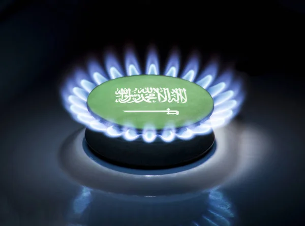 Burning gas burner of a home stove in the middle of which is the flag of the country of Saudi Arabia. Gas import and export delivery concept, price per cubic meter, transit, background, gasoline
