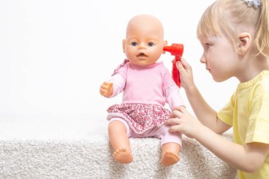 Küçük bir kız, bir bebekle oynar ve kulaklarını muayene eder. Çocuklarda pediatrik otolaringoloji, otitis medyasının tedavisi ve sülfür kapsülleri kavramı, kopyalama alanı
