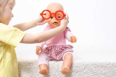 Çocuk bir bebekle oynar ve oyuncak gözlük takar. Pediatrik optalmoloji, gözlük seçimi ve çocuklarda görme bozukluğu tedavisi kavramı