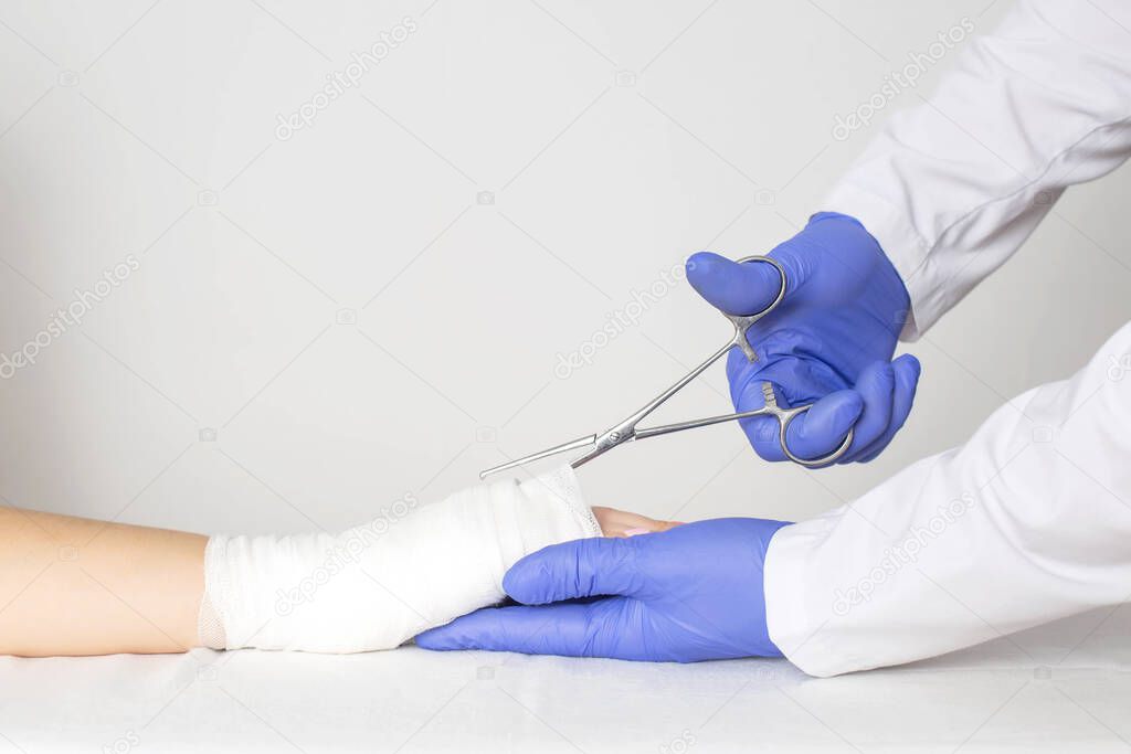 An orthopedic doctor removes plaster from bandages in the palm of a girl using medical scissors. Concept of bruise and fracture of the palm of the hand, copy space