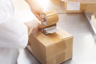 İşçi, fabrikada, sanayide, imalatta bitmiş malların olduğu karton kutuları paketliyor.