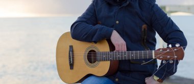 Genç adam deniz kıyısındaki gitar çalmak.