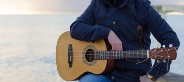 Genç adam deniz kıyısındaki gitar çalmak.