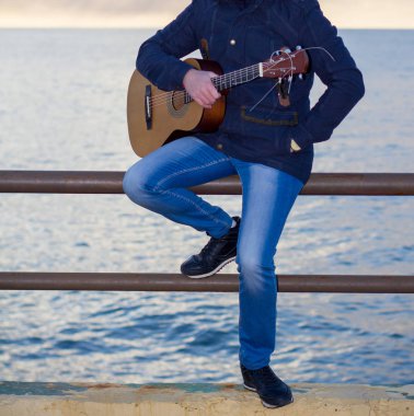 Genç adam deniz kıyısındaki gitar çalmak.