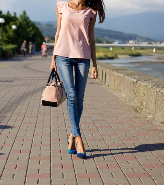 ピンクのブラウスと青いジーンズの女の子と堤防の上を歩くハンドバッグ — ストック写真