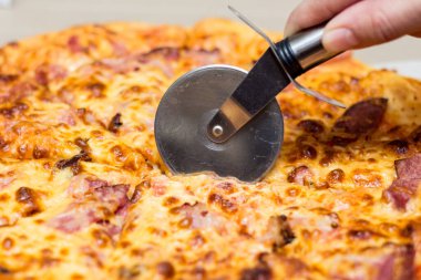 Jambonlu pizzayla yuvarlak bir bıçakla kesilmiş.,