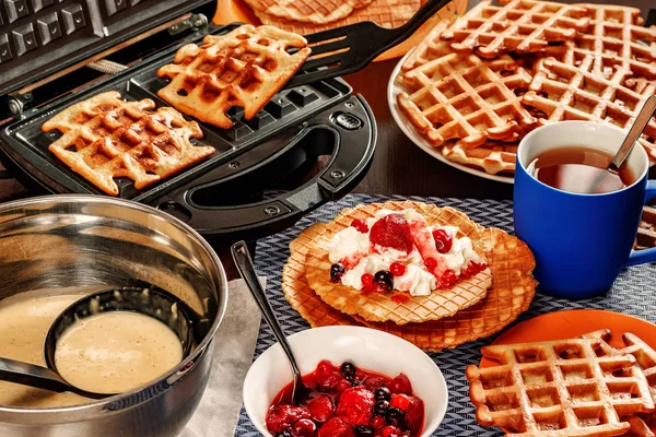 Waffles with whipped cream, berries and tea. Waffles are fried from dough in a waffle maker.