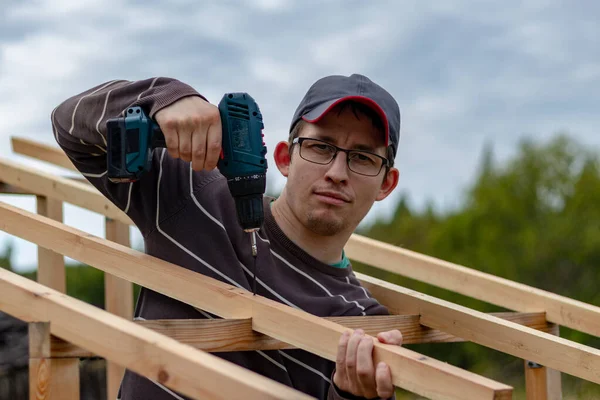 The builder screws the wooden rafter rafters with self-tapping screws with a cordless screwdriver