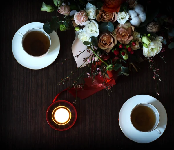 Valentines Day romantic background with flowers, cups of tea and candle. Bouquet over wooden table background. Backdrop with copy space. Place for text. Table for two.