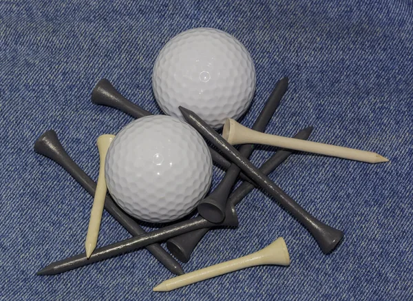 Two golf balls and a number of tees on a denim background.