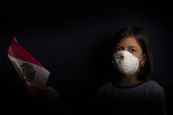 Portrait of little Peruvian girl wearing medical mask and holding hopefully the flag of Peru