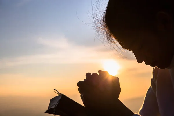 Silueta de la joven cristiana rezando con una cruz y op — Foto de Stock