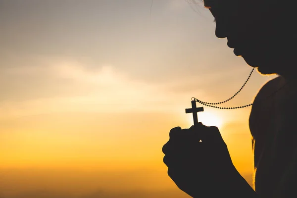 Silueta de la joven cristiana rezando con una cruz al sol — Foto de Stock