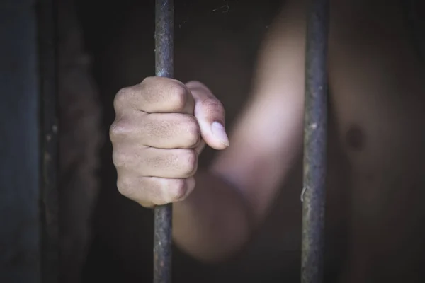 The hopeless hand of a man holds a metal cage in a dark room., h — Stock Photo, Image