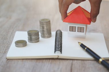 İnsan eli ev modelini madeni para yığınına koyar, tasarruf yapmayı planlar.
